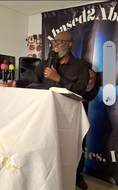 A man speaking at a podium with microphones and a banner in the background.